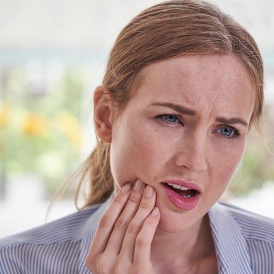 Woman who needs dental crowns in Arvada holding her jaw