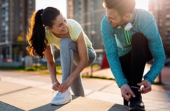 Couple with dental implant tooth replacement smiling outside while tying their shoes