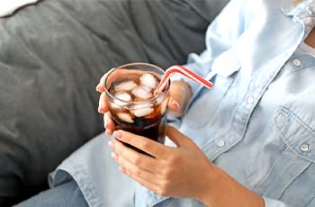Woman drinking glass of soda with ice cubes in it