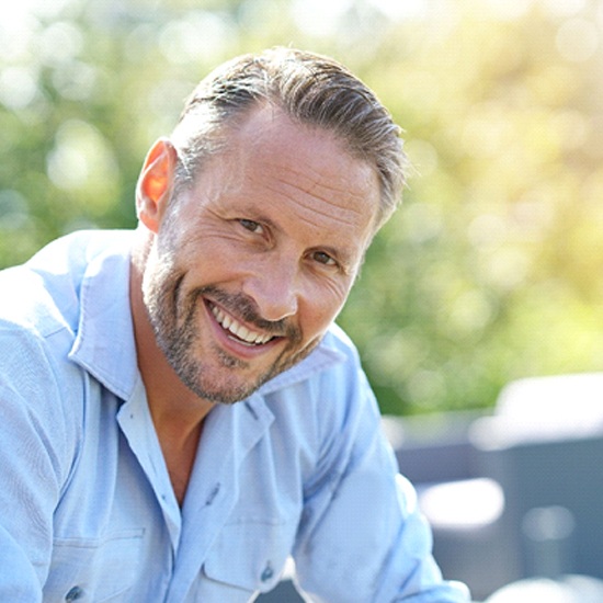 Older man with dental implants in Arvada smiling outside