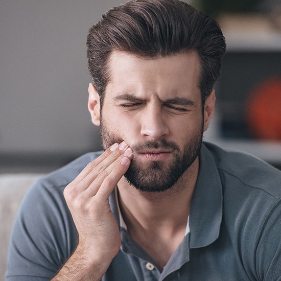 Man sitting on couch rubbing his cheek