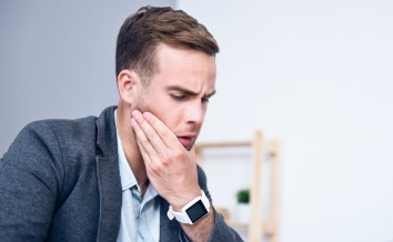 Man in need of wisdom tooth extraction holding jaw