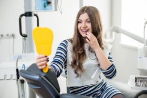 Smiling female patient looking in dentist’s mirror